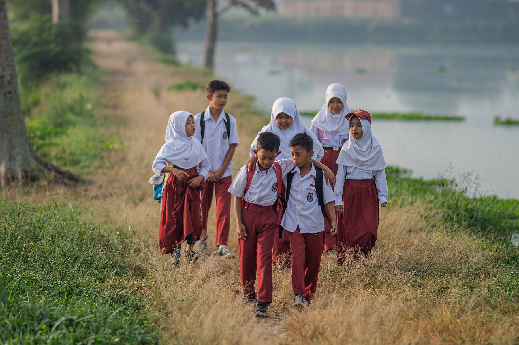 Anak-anak SD berseragam putih-merah berjalan pulang sekolah di tepi danau