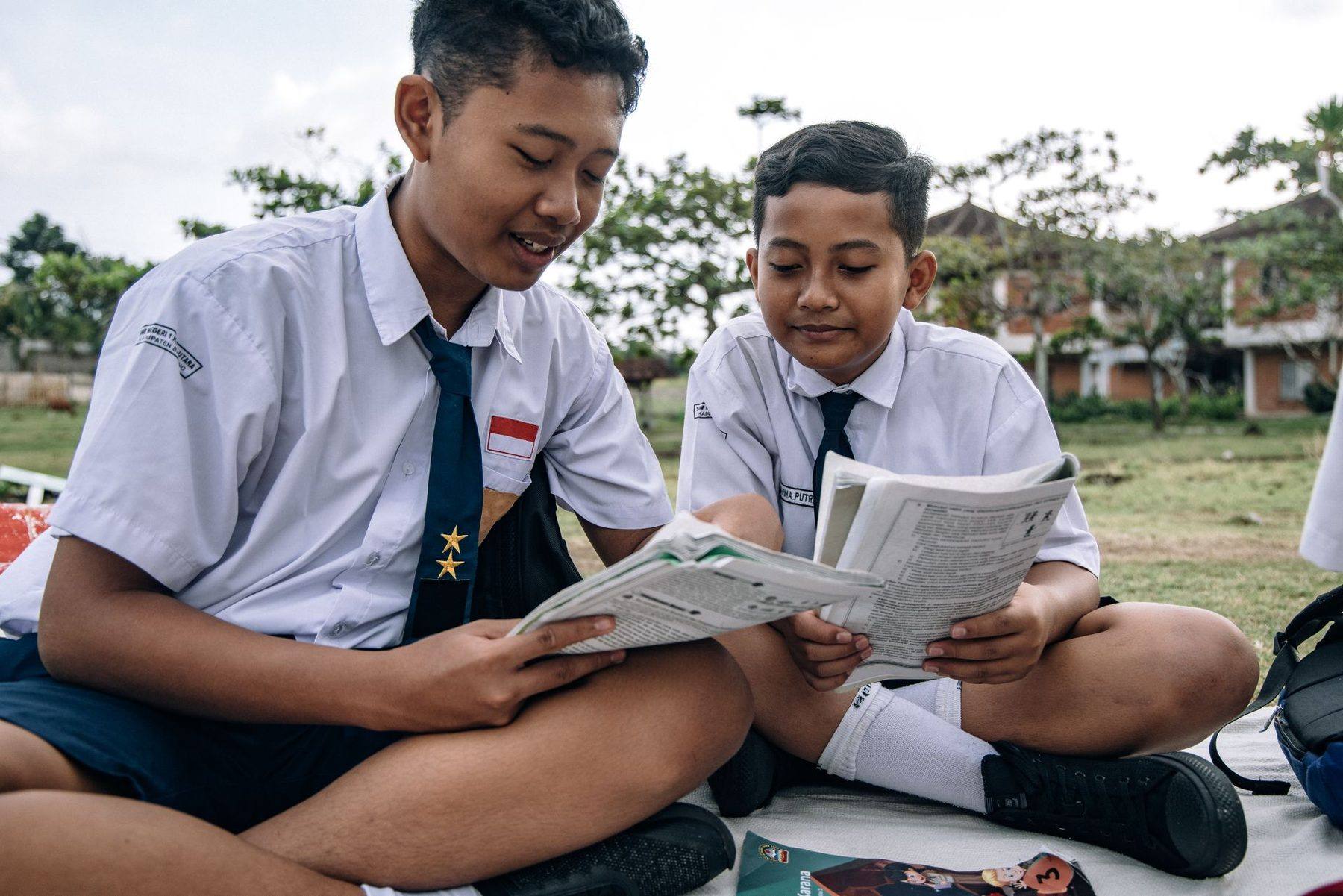 Dua siswa berseragam putih-biru membaca buku di lapangan